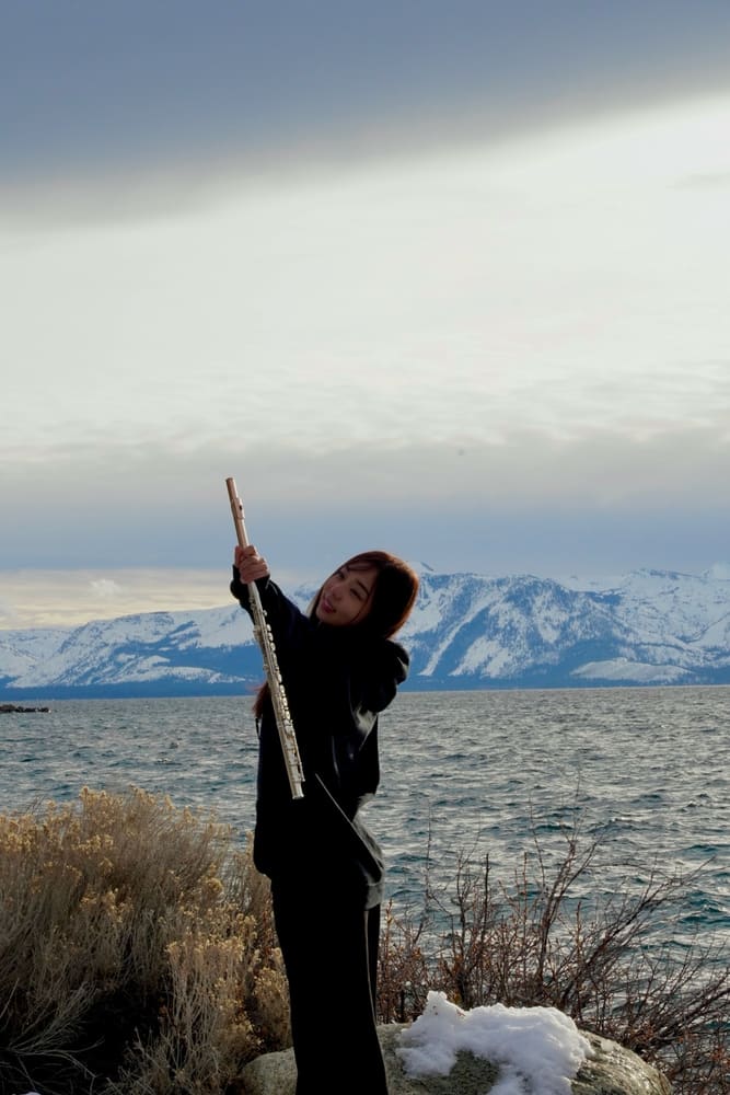 Monica raising her flute by a lake, snow-capped mountains behind