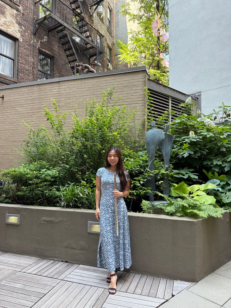 Monica in a blue floral dress in a garden courtyard