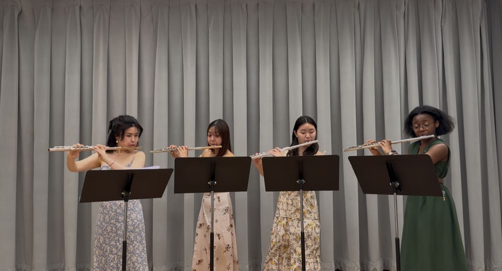 A flute quartet performing in front of a grey curtain
