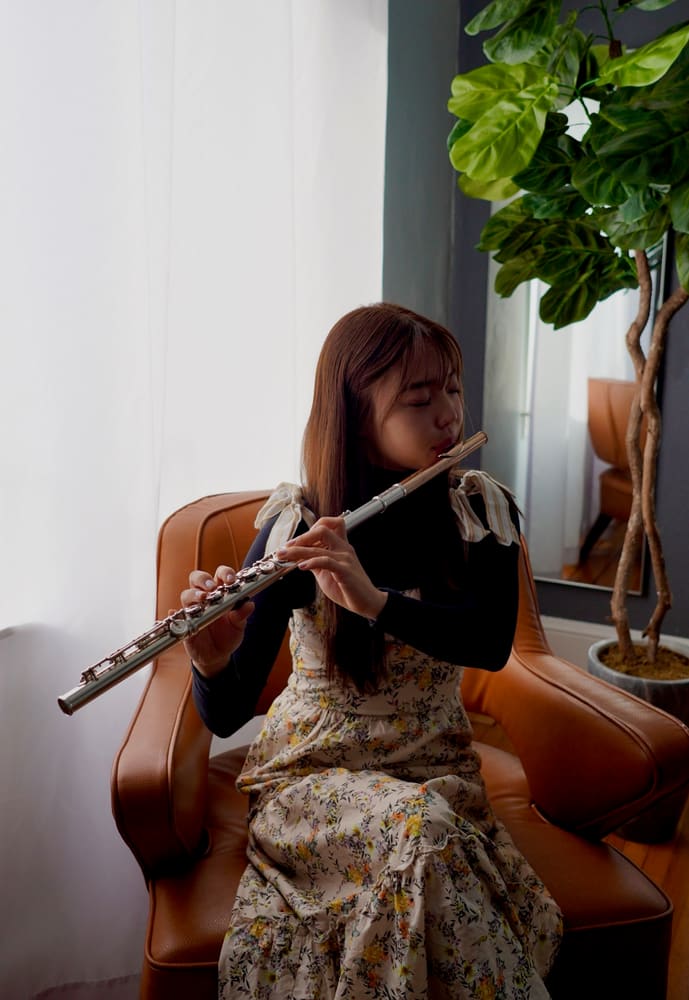 Monica playing the flute in a leather armchair