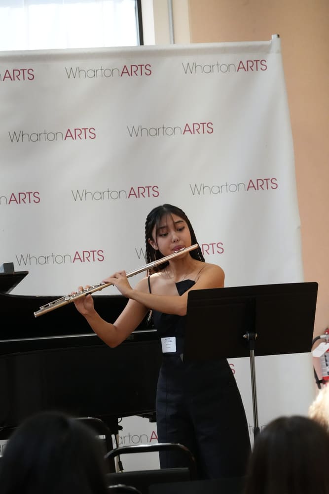 Monica performing at a music stand in front of a WhartonArts backdrop