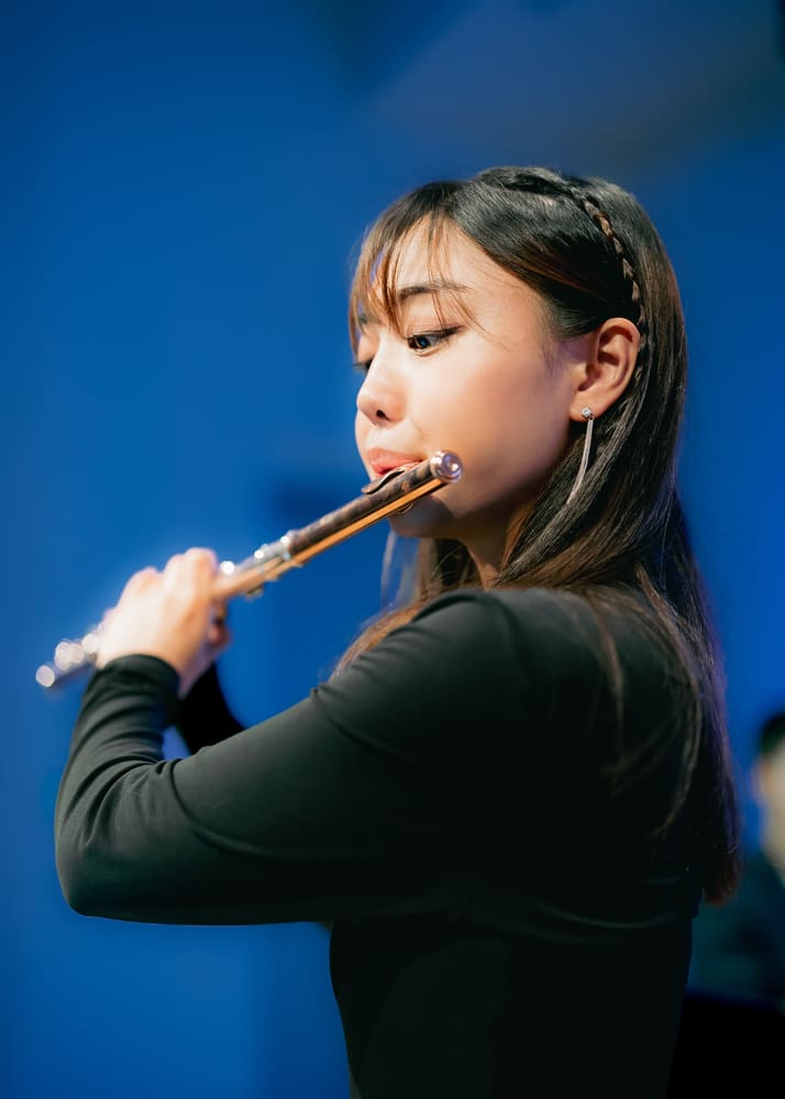 Close-up of Monica playing the flute against a blue background
