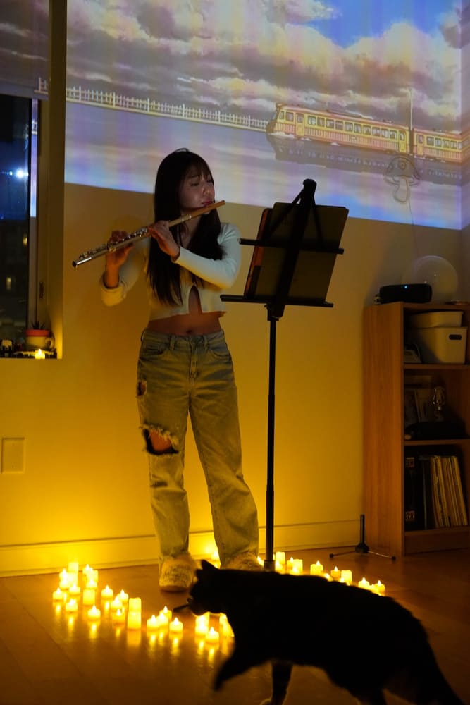 Monica playing the flute by candlelight, a cat in the foreground
