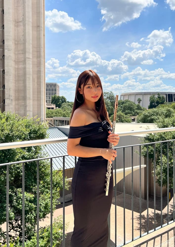 Monica holding her flute on a balcony under a blue sky