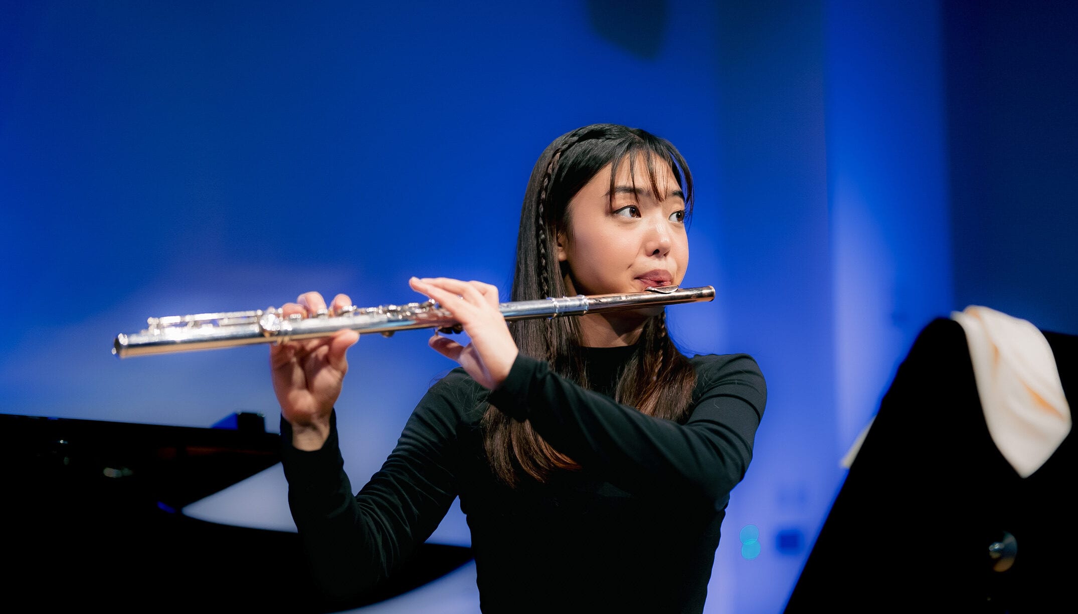 Monica Park playing the flute against a deep blue backdrop